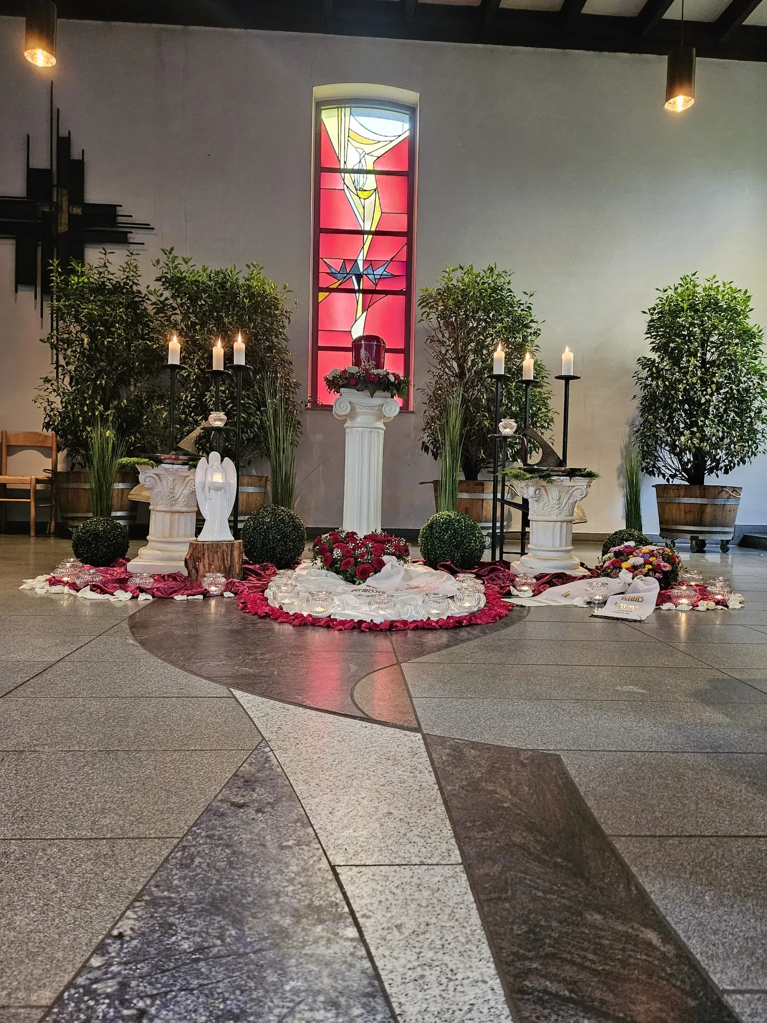 Würdevolle Trauerfeier in der Kapelle: Urne auf einer Säule vor rotem Kirchenfenster
