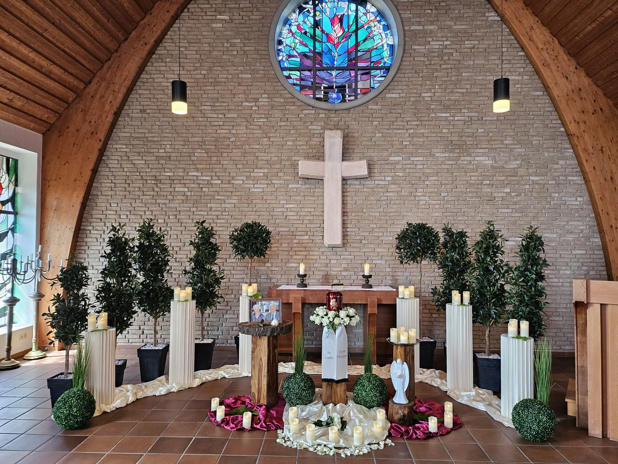 Trauerfeier in der Kapelle mit Urne, Kreuz und rundem Kirchenfenster