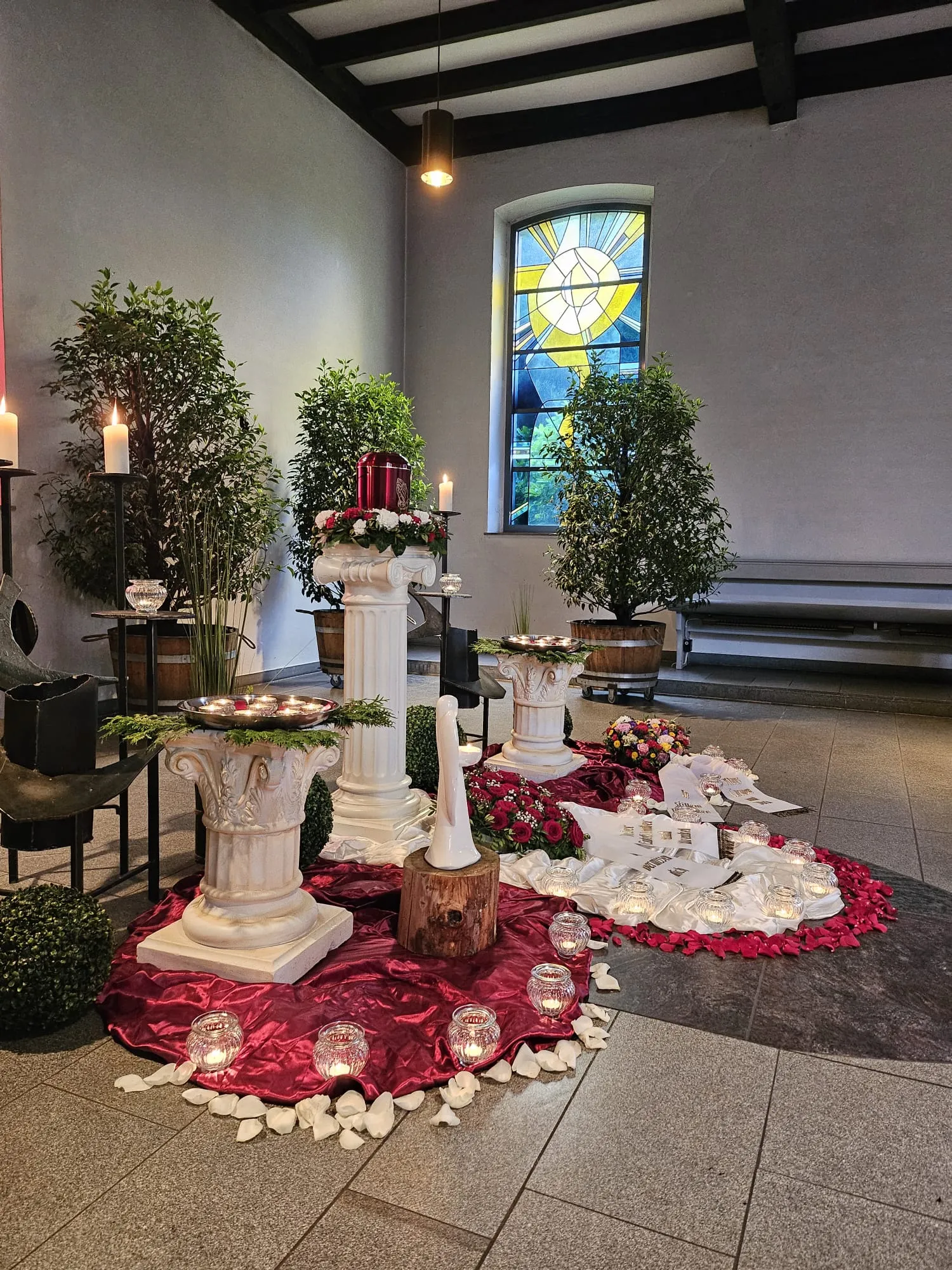 Trauerfeier in der Kapelle mit Urne auf Säulen, Kerzen und Rosenblättern