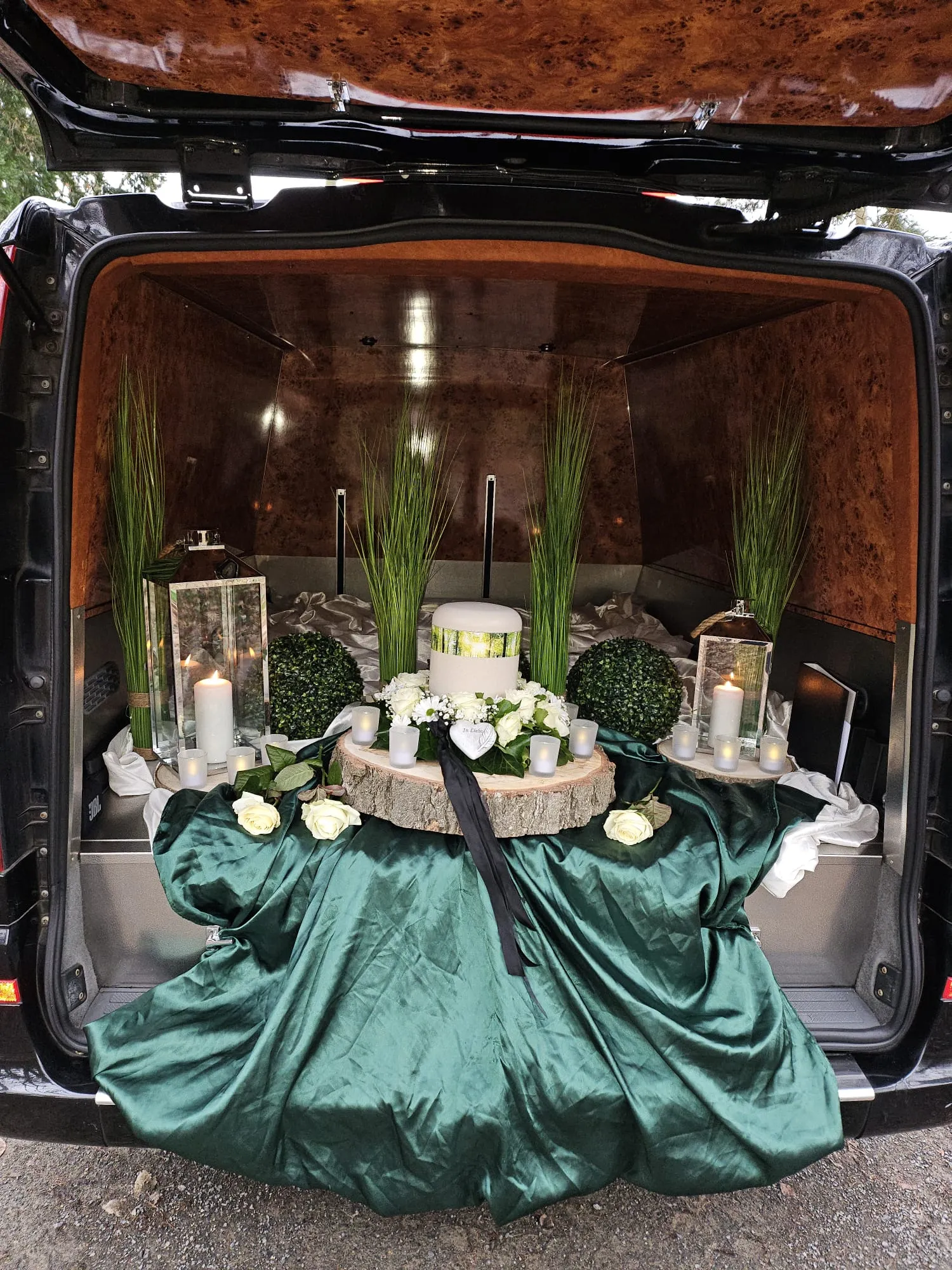 Würdevoll geschmückte Urne im Bestattungsfahrzeug mit grünem Tuch, Kerzen und Rosen