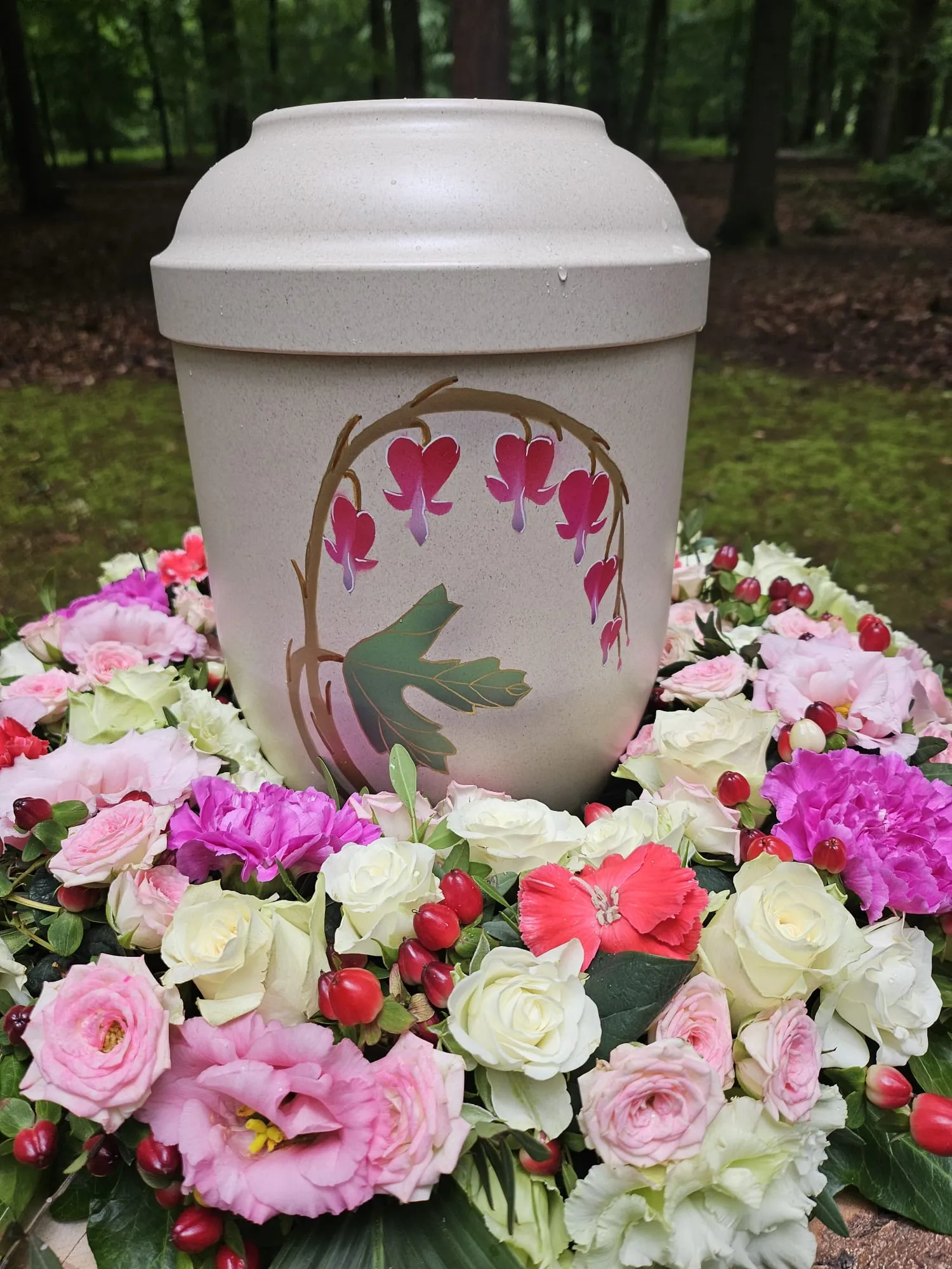 Urne mit Tränendes-Herz-Motiv in einem rosa-weißen Blumengesteck