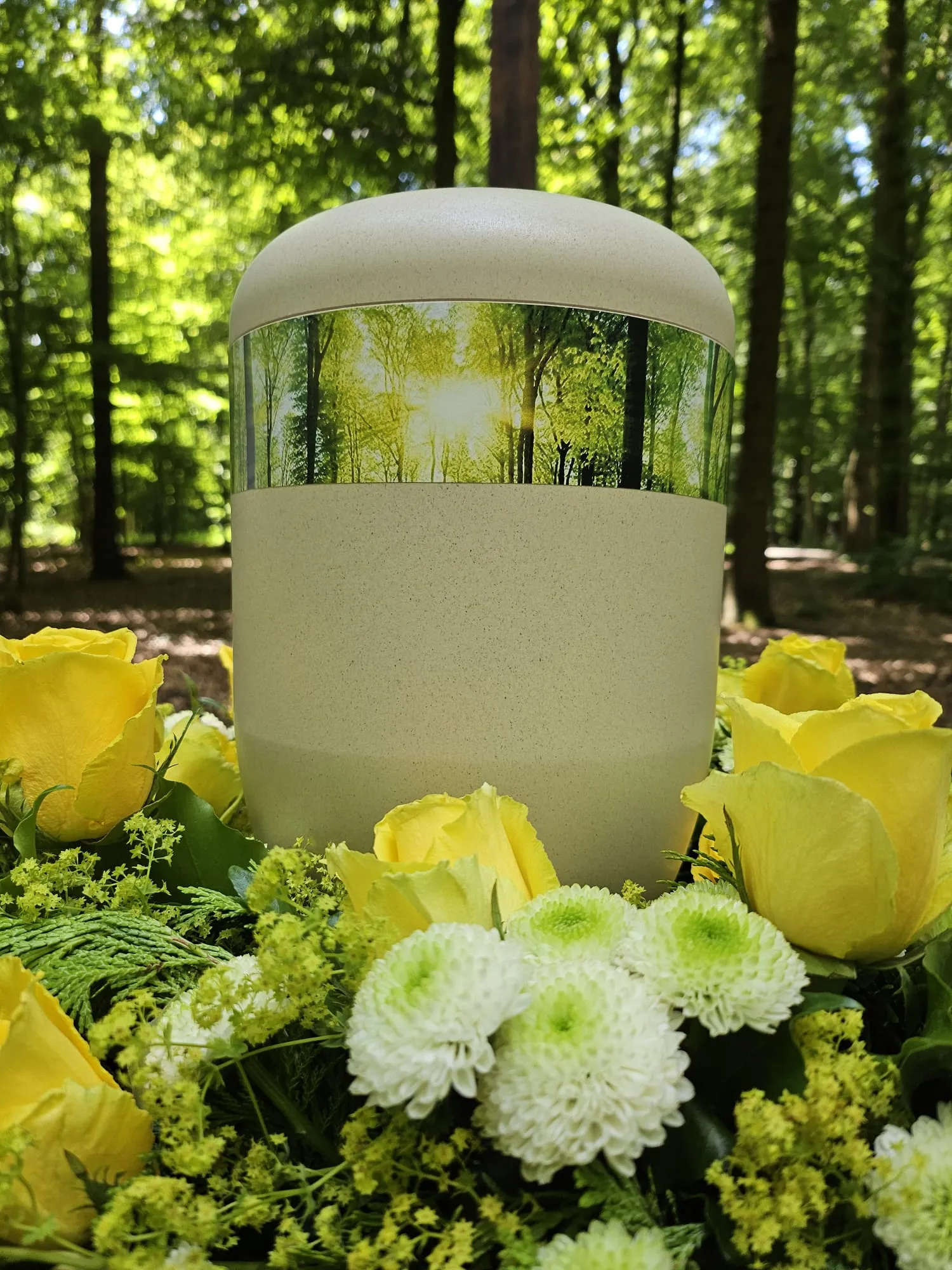 Bio-Urne mit Waldmotiv und gelben Rosen im sonnendurchfluteten Wald