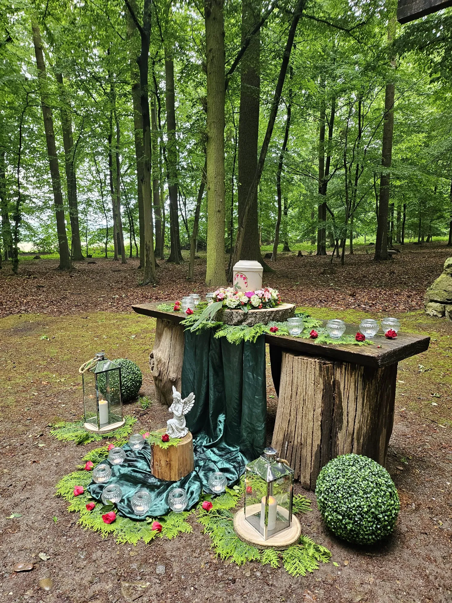 BaumFrieden-Zeremonie im Wald: Urne auf einem Baumstamm-Tisch mit Schutzengel und Laternen