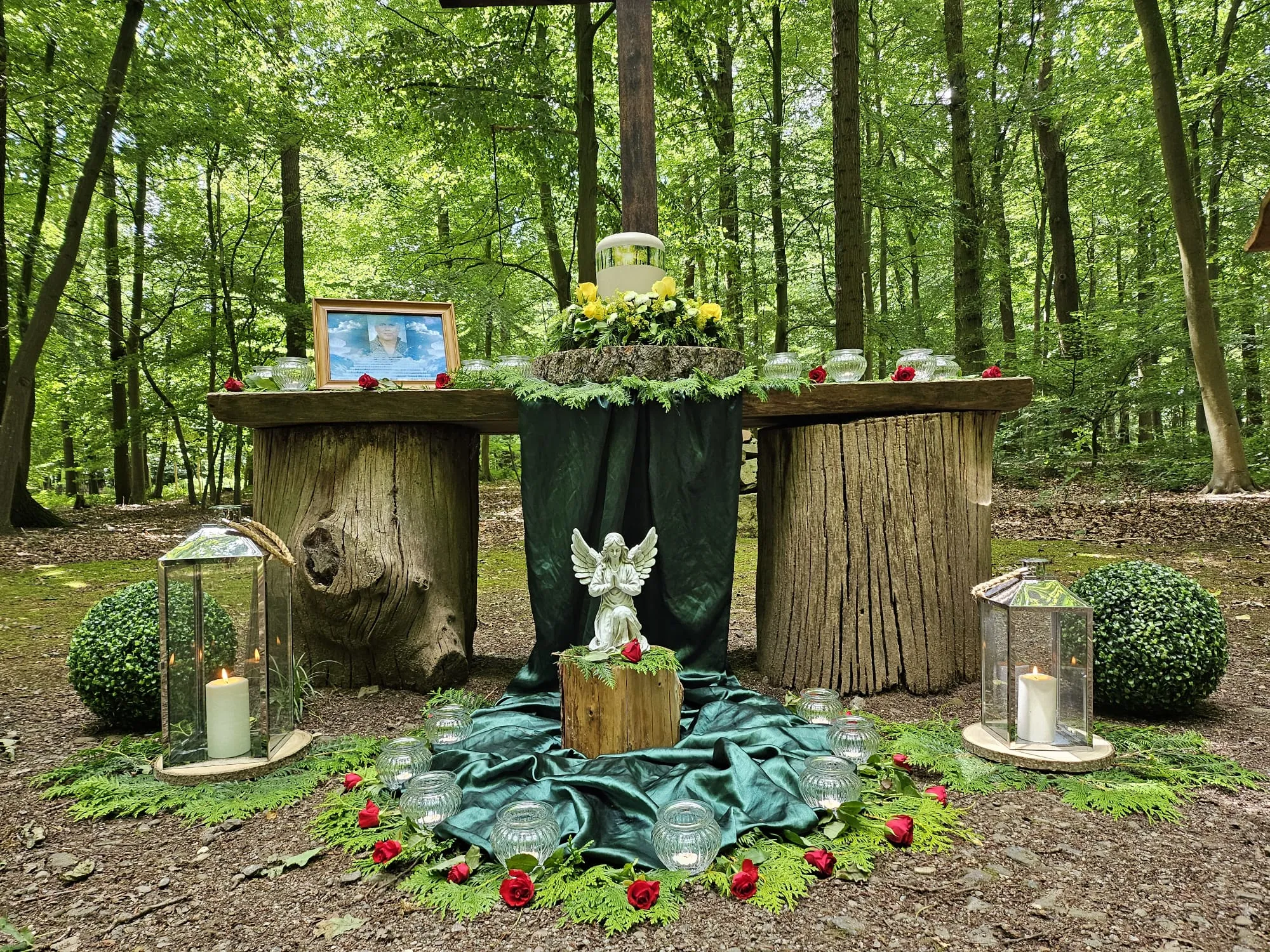 Waldzeremonie mit Baumstamm-Altar, Schutzengel-Figur und Kerzen im grünen Wald